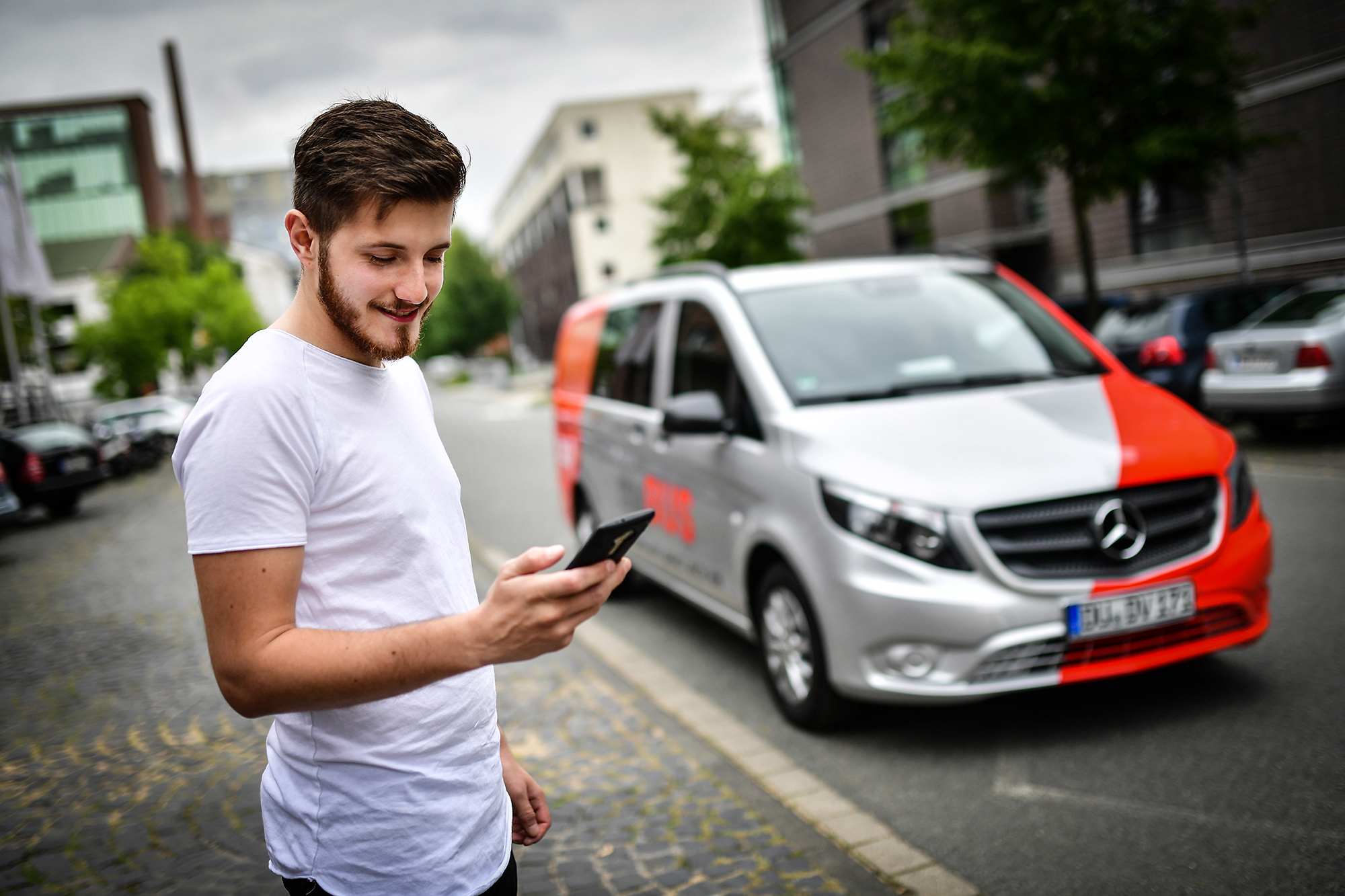 Junger Mann bestellt per Smartphone den myBUS-Dienst der DVG an der Straße