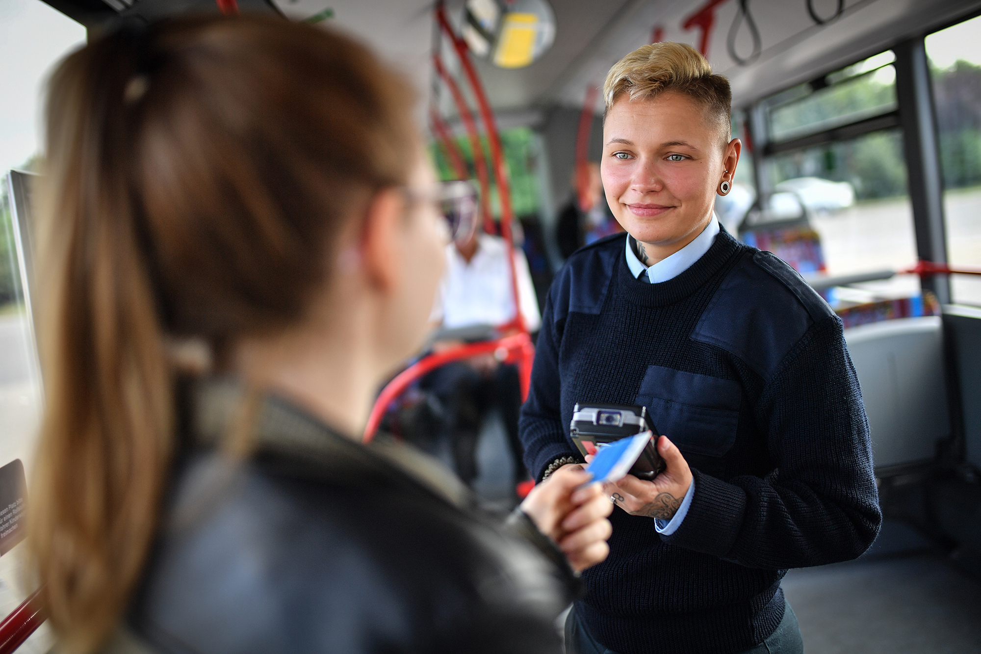 Kontrolleurin in Uniform prüft Fahrkarten in einem DVG-Bus.